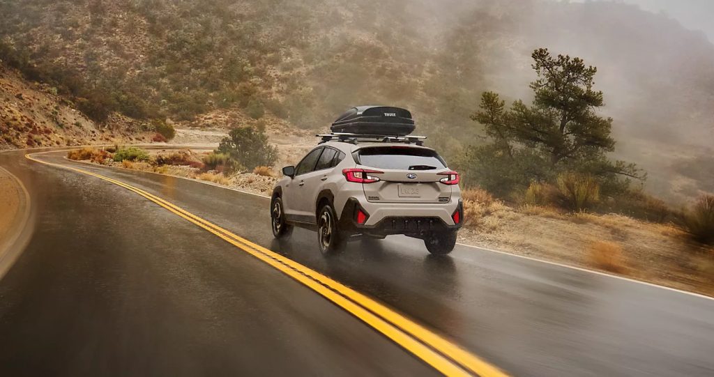2026 Subaru Crosstrek Hybrid SUV driving on rainy mountain road.